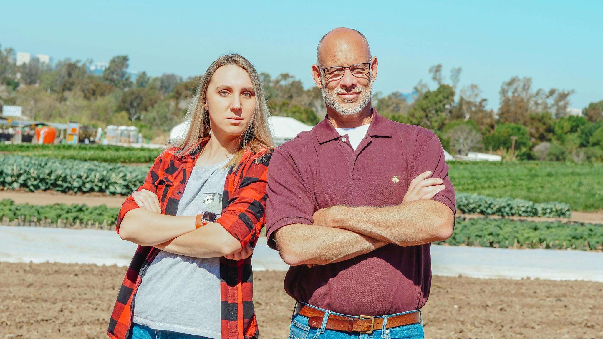 Portrait of male and female farmers confidently posing outdoors in a field.